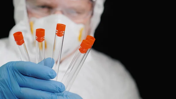 Um pesquisador em um terno protetor detém vários tubos de ensaio — Fotografia de Stock