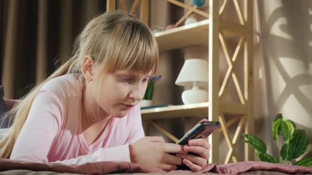 Das Kind ruht sich in seinem Zimmer aus, benutzt ein Smartphone — Stockvideo