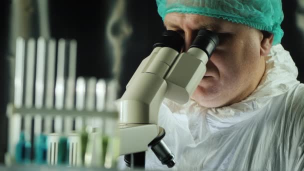 Reagens kémcsövek a laborban, a háttérben egy ember dolgozik egy mikroszkóppal — Stock videók