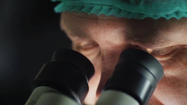 La cara de un investigador masculino mirando el ocular de un microscopio — Vídeos de Stock