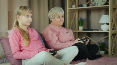 Aktif, yaşlı bir kadın video oyununda torunuyla oynuyor. Yatakta oyun kağıtlarının elinde oturuyor.