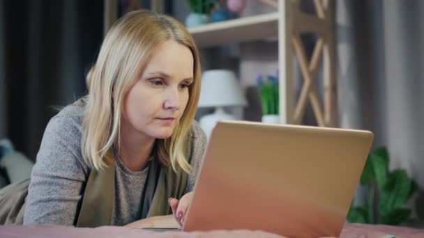 Vista lateral da mulher de meia-idade atraente trabalha com laptop em seu quarto — Vídeo de Stock