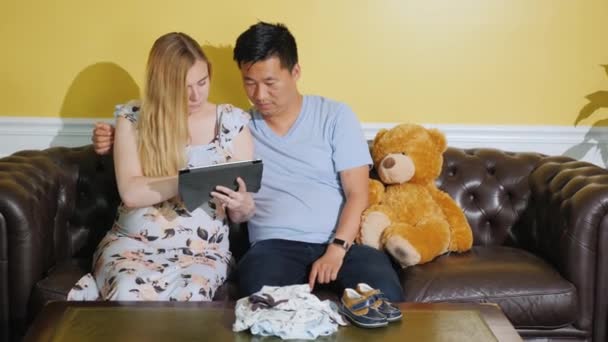 Eine junge Familie bestellt Kleidung für ihr zukünftiges Baby. Tablet nutzen — Stockvideo