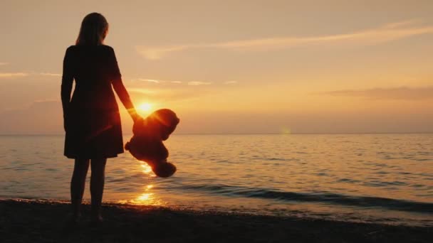 Eine einsame Frauenfigur am Meer hält einen Spielzeugbär in der Hand — Stockvideo