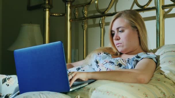 Young caucasian woman uses a laptop in her bedroom — Stock Video