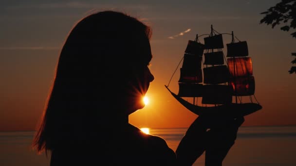 Profiel van een vrouw met een speelgoed zeilboot tegen de ondergaande zon — Stockvideo