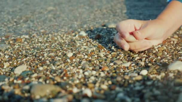 Una mano femminile tiene un sassolino sullo sfondo del surf . — Video Stock