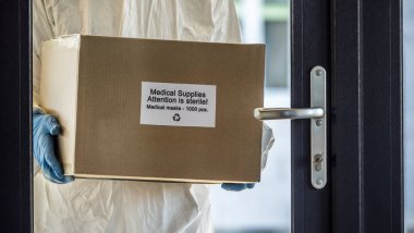 Antiviral giysili bir adam elinde koruyucu tıbbi maskelerle kapının önünde duruyor.