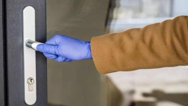 Eine Hand in einem Schutzhandschuh am Griff der Haustür. Schutz inmitten einer Epidemie — Stockfoto