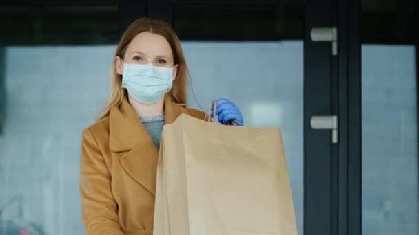 Frau mit Handschuhen und Maske mit Tüten voller Lebensmittel auf dem Hintergrund beim Betreten des Lebensmittelgeschäfts — Stockvideo