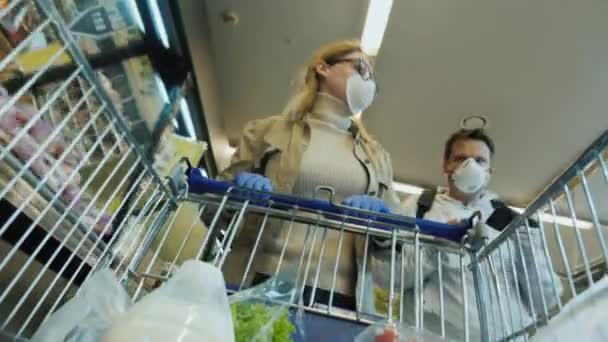 Ein Mann und eine Frau kaufen während der Coronavirus-Epidemie Lebensmittel. Schutzmasken und Handschuhe tragen — Stockvideo
