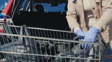 Koruyucu eldivenli adam alışveriş torbalarını arabanın bagajına koydu.