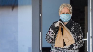 Maskeli, yemek torbası taşıyan yaşlı bir kadının portresi. Karantinada eve teslim