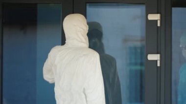 Koruyucu kıyafetli bir kurye doktora değerli ilaçlarla dolu kırmızı bir çanta verir.