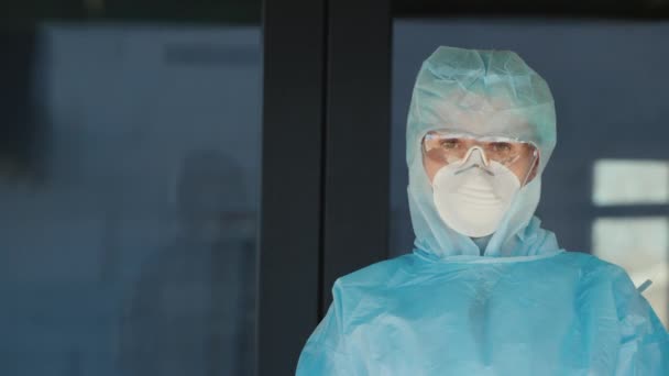 Portret van een vermoeide vrouwelijke arts voor de deur van de kliniek. In een beschermend pak en masker — Stockvideo