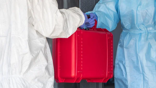 Een koerier in een beschermend pak geeft de dokter een rode doos met waardevolle medicijnen — Stockfoto