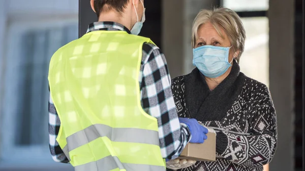 Postacı salgın sırasında yaşlı kadınlara paket teslim ediyor.