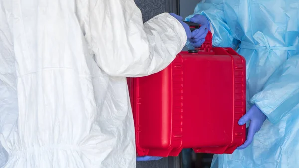 Een koerier in een beschermend pak geeft de dokter een rode doos met waardevolle medicijnen — Stockfoto