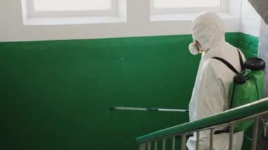 Koruyucu giysili bir adam odaya antiseptikle bakıyor.