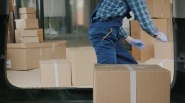 Tıbbi maskeli ve eldivenli bir kargo adamı arabanın bagajına ilaç kutularını dolduruyor.