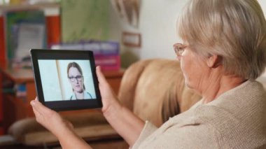 Yaşlı kadın video bağlantısı üzerinden aile doktoruna danışıyor, elinde tablet var