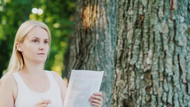 Молодая женщина прикрепляет объявление к дереву в парке — стоковое видео