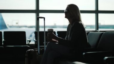 Bir iş kadını havaalanı terminalinde kağıt bardaktan kahve içiyor. Yolcu uçağı bekliyor.