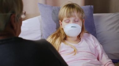 Yaşlı bir kadın, maske takan hasta bir çocuğun yanında oturuyor.