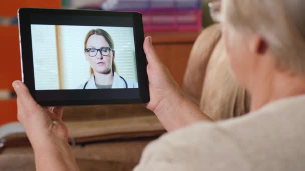 Starsza dorosła kobieta konsultuje się z lekarzem rodzinnym przez łącze wideo, trzyma tabletkę — Wideo stockowe