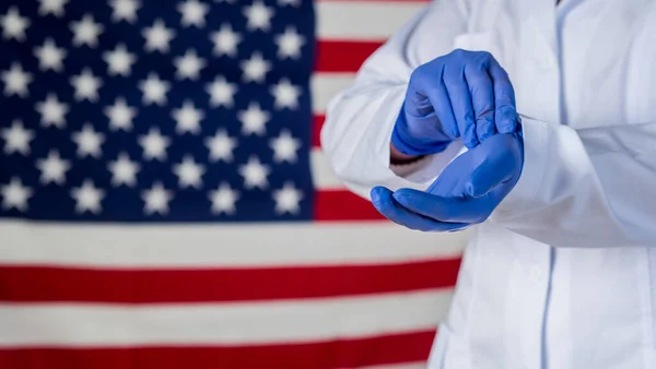 Arzt trägt Schutzhandschuhe gegen amerikanische Flagge — Stockfoto