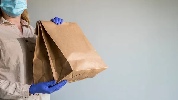 Een man met beschermende handschoenen en een masker houdt pakjes voedsel bij zich thuis. — Stockfoto
