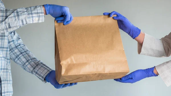 Breng de zak voedsel over in beschermende handschoenen. Voedsellevering — Stockfoto