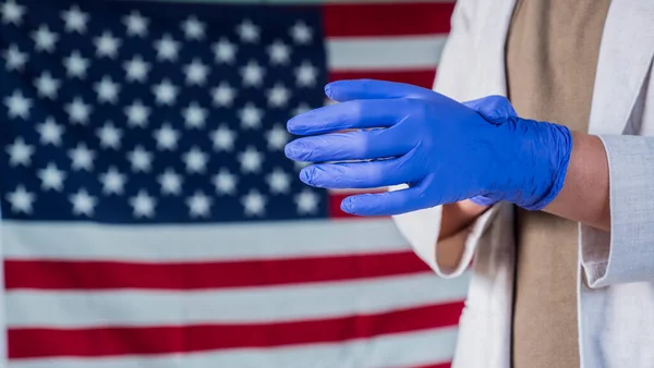 Чоловік носить захисні латексні рукавички проти американського прапора. — стокове фото