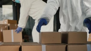 Koruyucu elbiseli insanlar kutularla dolu bir minibüsü boşaltıyor. İlaç ve ekipman teslimatı.