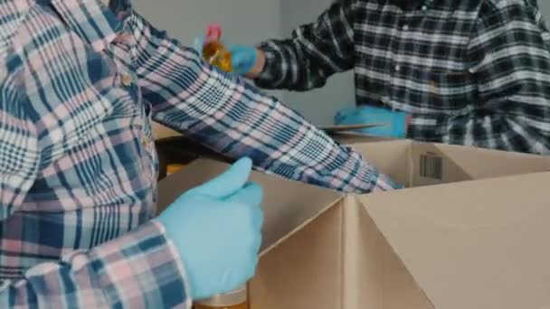 Voluntarios empacan comida en cajas de cartón, guantes y máscaras médicas — Vídeos de Stock