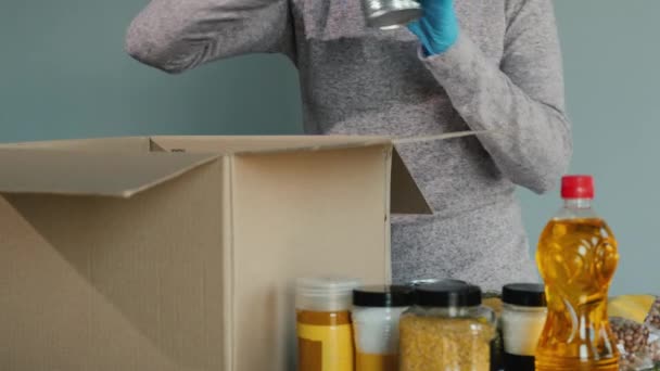 Voluntario en guantes de protección pone comida en una caja de cartón — Vídeos de Stock