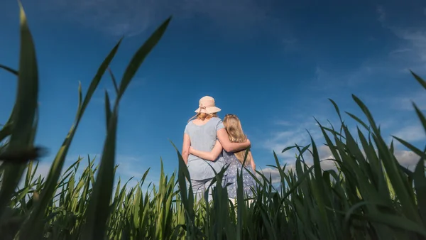 Moeder knuffelt dochter, staan op een mooie groene weide tegen een heldere blauwe lucht — Stockfoto