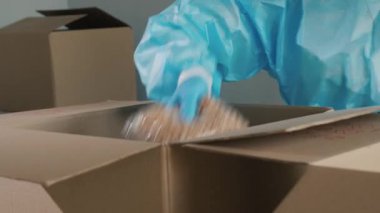 Koruyucu giysili bir adam uzun süreli ürünleri bir kutuya koyar.