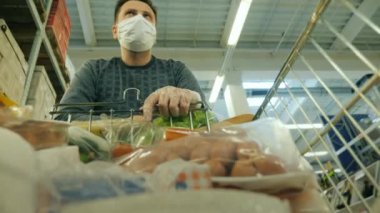 Koruyucu maskeli bir adam alışveriş arabasıyla dükkânda yürüyor.