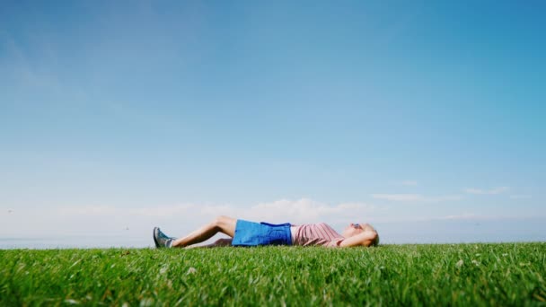 Een gelukkige vrouw ligt midden in een groene weide, ontspant en rust alleen in de natuur — Stockvideo