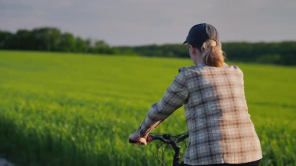 Frau fährt mit Fahrrad zwischen grünen Weizenfeldern — Stockvideo