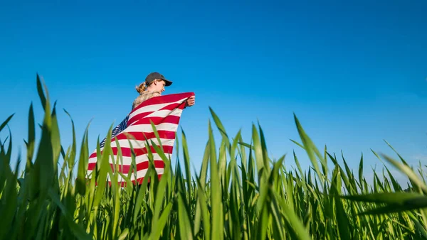 Um agricultor com uma bandeira dos EUA em seus ombros está em um campo de trigo verde — Fotografia de Stock