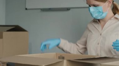 Maskeli ve eldivenli bir kadın karton kutulara yiyecek koyar.