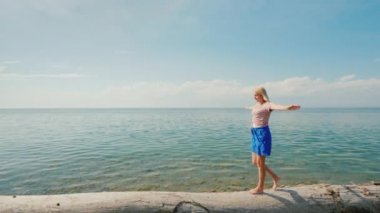 Odaklanmış bir kadın kütük boyunca yürür, elleriyle dengesini korur.
