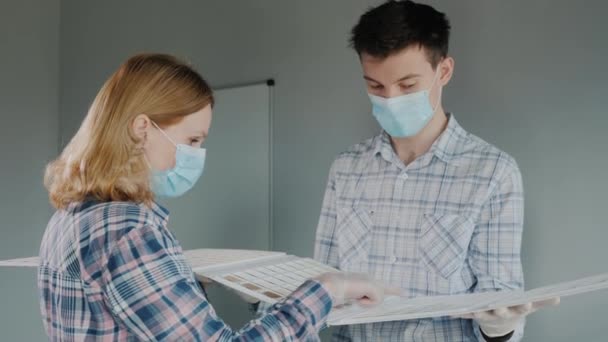 The designer shows samples of materials to the customer, both wear protective masks — Stock Video