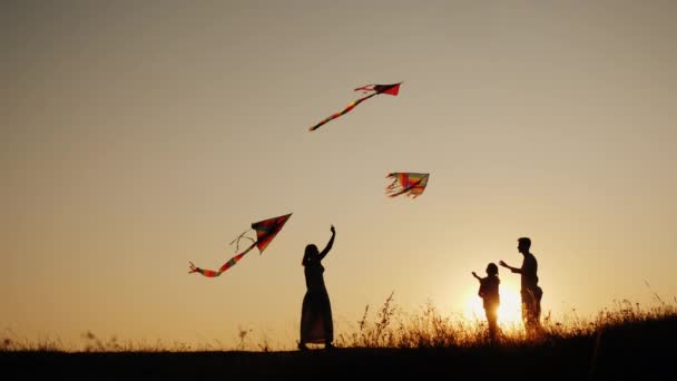 En ung sam med två barn leker drakar vid solnedgången på en pittoresk plats. Familjeaktivitet utomhus — Stockvideo