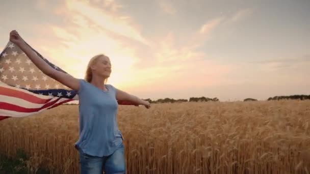 Счастливая женщина с флагом США бежит по пшеничному полю — стоковое видео