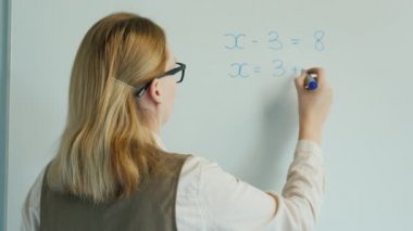 Arka görünüm: Öğretmen cebirde denklemi çözer. İlkokul için çevrimiçi dersler