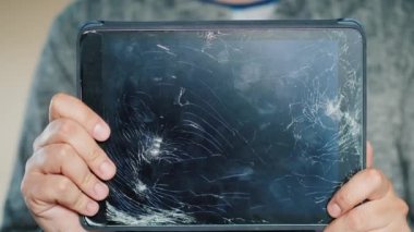 Bir adam kırık bir ekranla tablet tutuyor.