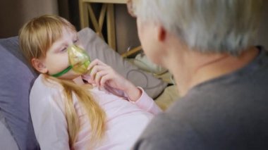 Soğuk bir çocuk özel bir maske takıyor, büyükannesinin yanında oturuyor.